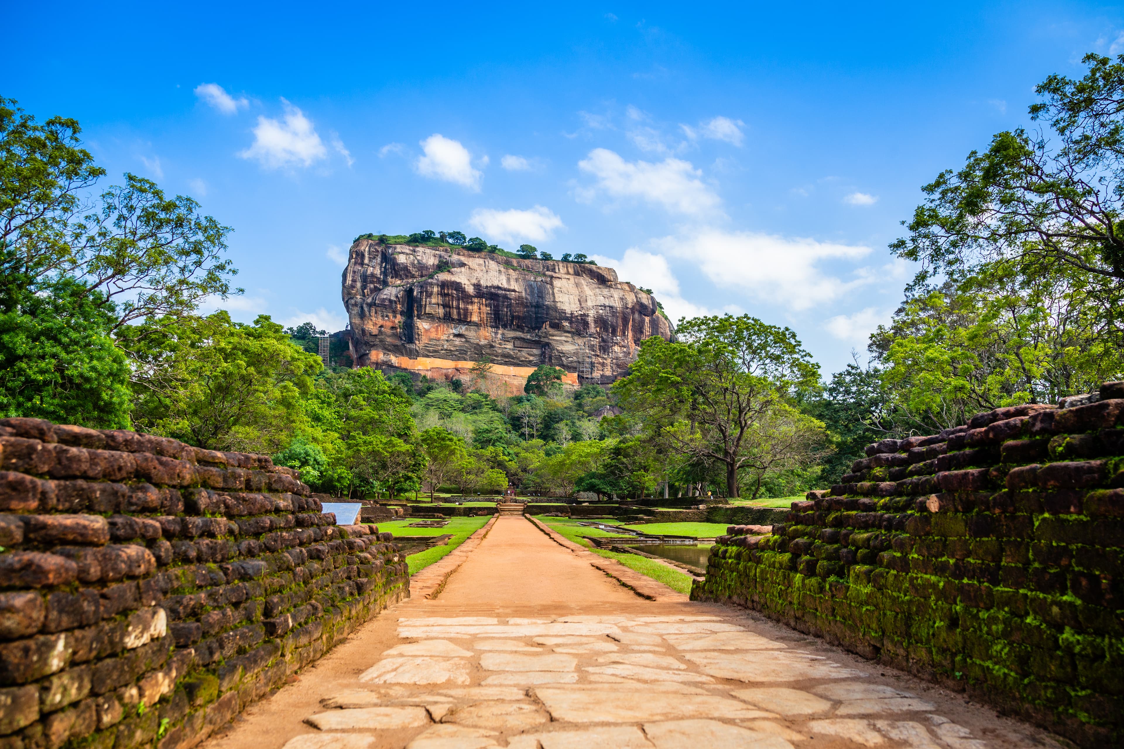 Ancient stone pathway through ruins leading to Sigiriya Lion Rock Fortress under vivid blue sky, Sri Lanka